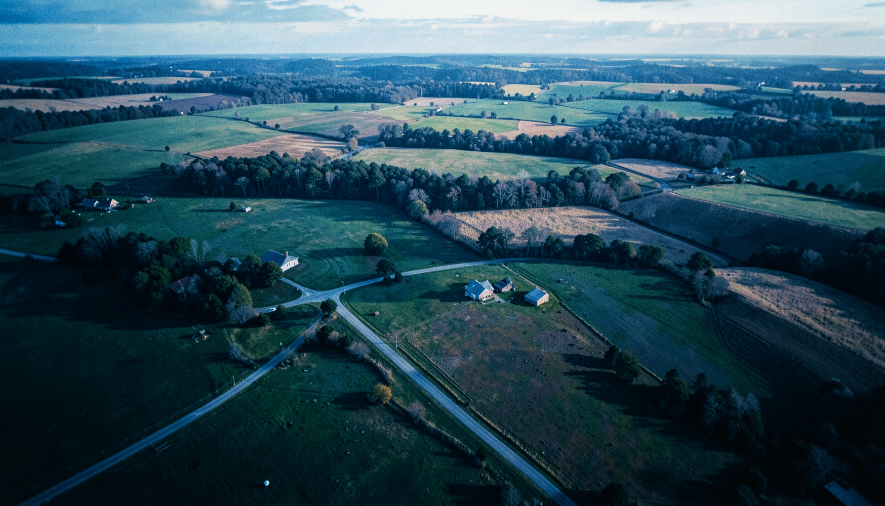 Aerial view of a rural Tennessee landscape with winding roads, scattered farm buildings, and patchwork fields under soft afternoon light